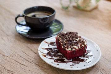 A piece of red velvet cake with coffee cup on wooden table in cafe