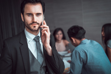 businessman using smart phone at meeting room with his colleagues background. 
