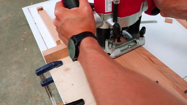 Tanned white male hand working with the milling router on a hard wood.