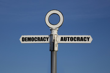 Old road sign with democracy and autocracy pointing in opposite directions against a blue sky