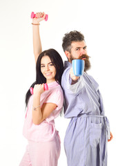 Morning alternative concept. Girl with dumbbell, man with coffee cup. Couple, family on sleepy faces, full of energy. Couple in love in pajama, bathrobe stand isolated on white background.