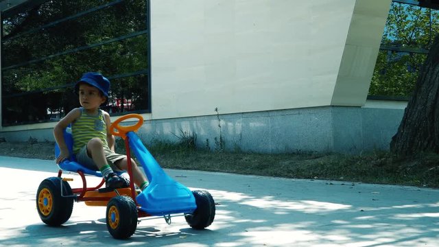 Little cute boy having fun driving a pedal car in the park. 4K