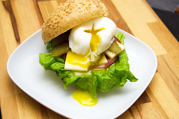 appetizing hamburger with green salad, meat and poached egg under a bun with sesame seeds