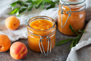 Jar of apricot jam with leaves and fruit on grey table