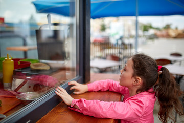 Fototapeta na wymiar Curious little girl waiting for her burger in the street shop window.