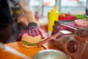 Chef in rubber gloves making burger in street cart, shallow depth of field.