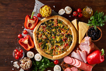 Pizza still life. Freshly baked pizza and its components arranged on wooden background.