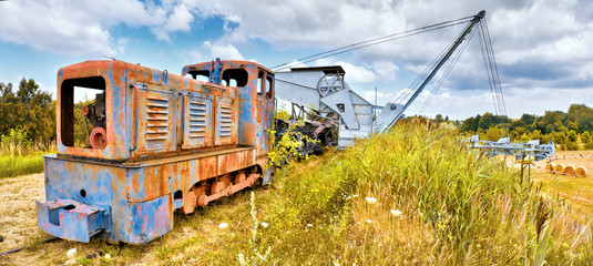 Old Rusty locomotive and bucket chain excavator and a row of coal vagons on a grass hil