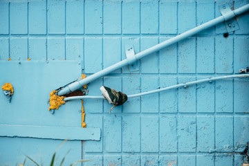Blue wall from tiles with cyan closed hatchway and pipes close up. Background of wall of building with copy space.