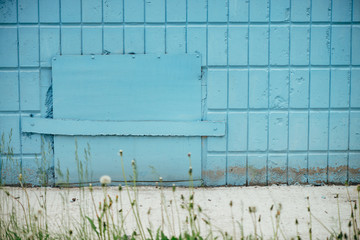 Blue hatchway in wall of building close up with copy space. Background of cyan closed hatch on tiles with grass on foreground.