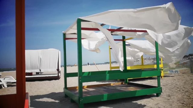 Slow motion video of sheds awning with white curtains on the seashore in the wind.