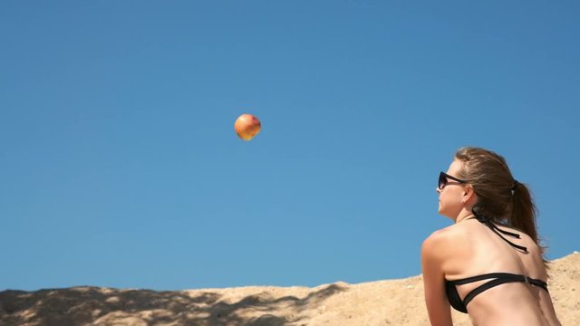 Slow motion: Sexy young girl in a black swimsuit and glasses, destroys fruits and vegetables with a baseball bat. It is located on a sandy beach near the sea in summer. Breaks the apple