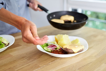 Female hands, black frying pan, boiled potatoes, green salad, meat cutlet with cheese, white ceramic dish on wooden table. Woman puts food on plates. Homemade dinner for the whole family