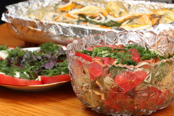 Fototapeta na wymiar Glass bowls with salads and bowl with aluminum foil with marinated hake with potatoes and spices baked in the oven