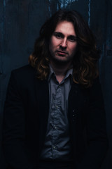 Fototapeta premium portrait of a handsome man in a black jacket with long hair on a dark background, serious facial expression
