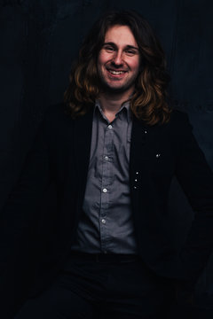 portrait of a handsome man in a black jacket with long hair on a dark background, the man smiles.
