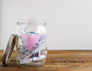 Einmachglas mit rosa Herz und zusammengerollten Notizzetteln, weißer Hintergrund, Textfreiraum