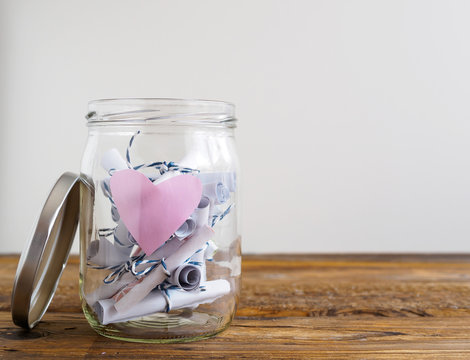 Einmachglas mit rosa Herz und zusammengerollten Notizzetteln, wei&szlig;er Hintergrund, Textfreiraum