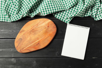 Blank sheet of opened notepad and kitchen utensils on  table with tablecloth, copy space