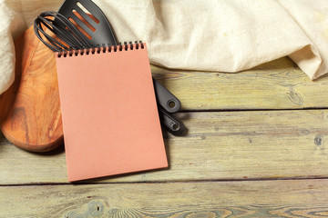 Blank sheet of opened notepad and kitchen utensils on  table with tablecloth, copy space