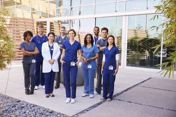 Healthcare team with ID badges stand outdoors, full length