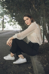  portrait of a beautiful dark-haired girl in a forest park in a white shirt and dark trousers