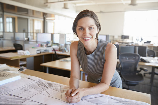 Young female architect leaning on desk smiling to camera