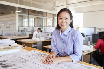 Female Asian architect smiling to camera in open plan office
