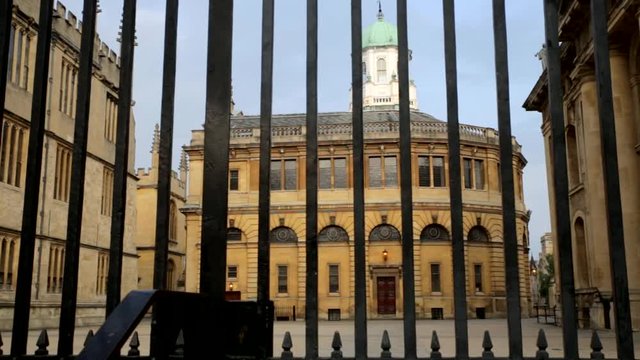 Sheldonian Theatre, Bodleian and Clarendon Building looking through iron railings from Catte Street, dolly slider to left, early morning