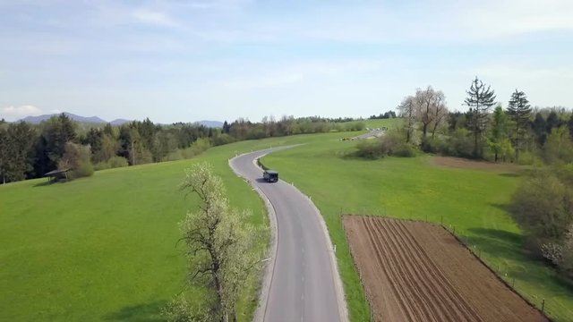 A black van is driving uphill on the country road. Aerial shot.