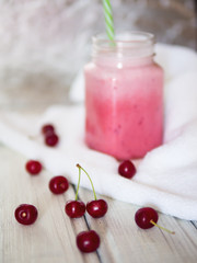 Cherry smoothies with fresh cherries on a wooden table.