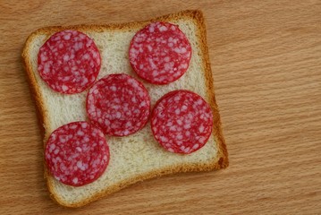square piece of bread and sliced sausage salami on a brown table
