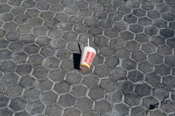 Minimalistic picture of a cardboard grass of a junk drink from a fast food company discarded and forgotten on the street.