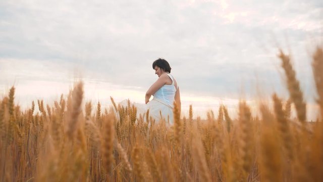 Plus size fashion model in slow motion video walking white dress on field wheat. fat woman on nature in the field grass flowers summer lifestyle. agriculture overweight female body. full girl length