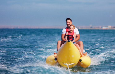 happy family, delighted father and son having fun, riding on banana boat during summer vacation