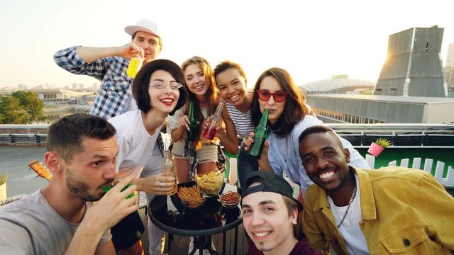 Point of view shot of young men and women taking selfie with bottles, enjoying soft drinks, drinking and posing with funny faces. Modern lifestyle and beverage concept.
