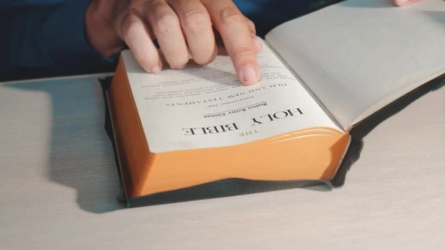 Holy Bible. Man preacher praying to God with his hands resting on a bible slow motion video. the man is reading a book Holy lifestyle Bible in church. concept for faith spirituality holy bible and
