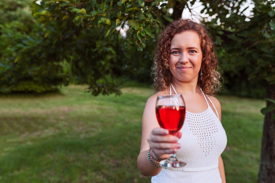 Portrait of a beautiful curly woman holding a glass of wine and offer by a glass of wine
