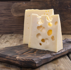 Cheese with holes is cut into portions on a wooden board, a useful dairy product. Tasty food. Country style photo. Place for text. Copy space.