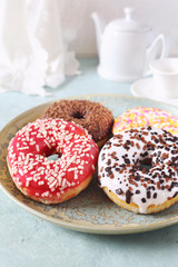 Four variegated sweet donuts and teapot for breakfast