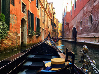 Venetian gondola crossing a narrow canal with traditional Venetian hat, passenger point of view