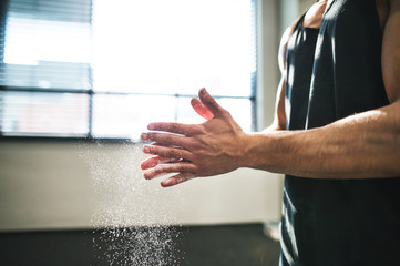 Fit young man in gym smears his hands with magnesium. Close up.