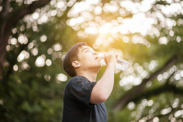 Thai man drinking water with his eyes closed after exercises.plastic bottle of water after workout outdoors.Outdoor portrait of handsome young man drinking water on court..