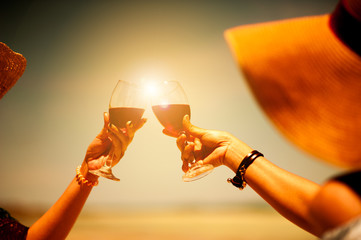 People holding glasses of red wine making a toast at the beach picnic on summer.friends toasting...