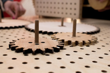 Naklejka na ściany i meble Gear wheels of wooden gears on a perforated table assembled together to form a mechanism. Educational activity for children, STEM subjects for engineering and mechanics at school