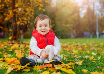 happy little girl 3 years old sitting surrounded by yellow fallen leaves