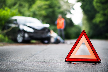 A close up of a red emergency triangle on the road in front of a car after an accident. - obrazy, fototapety, plakaty