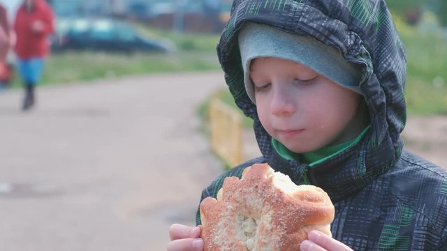 Boy eating a bun on the street.