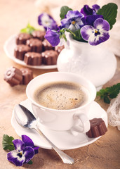 Postcard with cup of cooffee, chocolate candies in flower shape and pansy. Holiday food concept. Retro style toned.