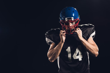 american football player putting on helmet and looking at camera isolated on black © LIGHTFIELD STUDIOS